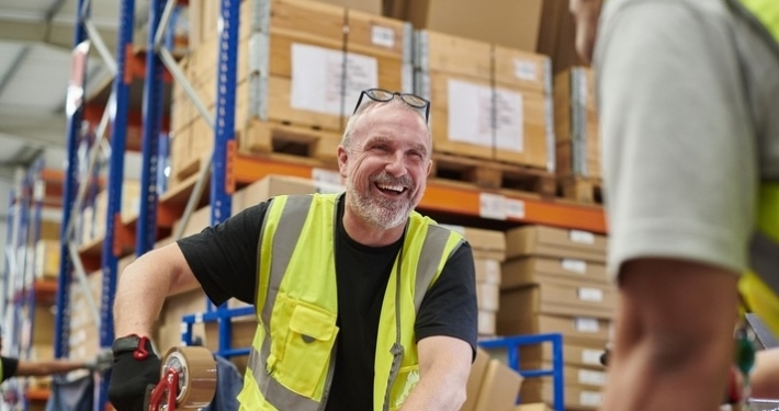 Warehouse worker in a yellow safety vest taping a box