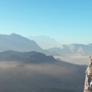 Hiker with a backpack on a cliff looking at mountains.