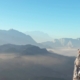 Hiker with a backpack on a cliff looking at mountains.
